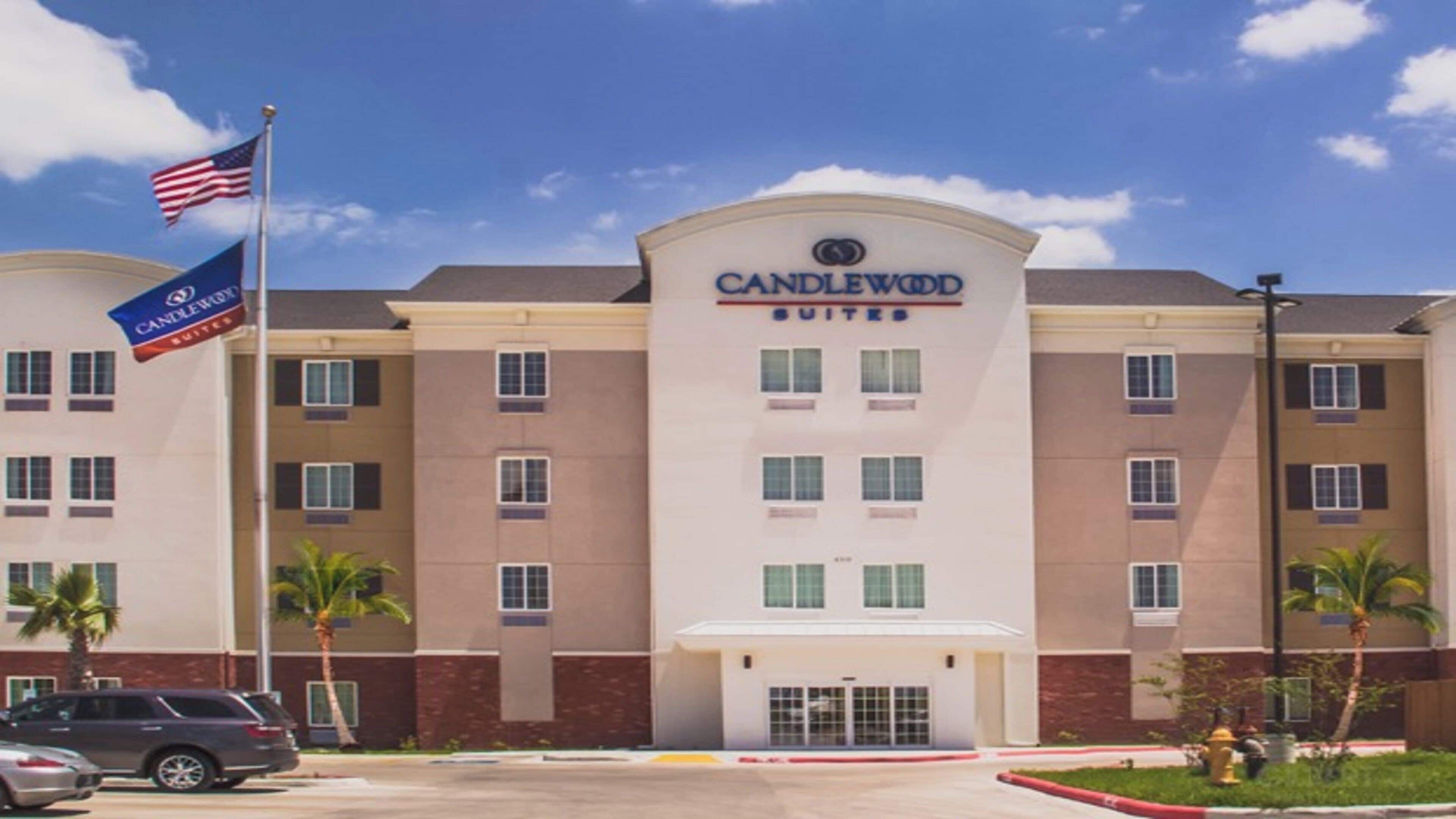 Un hotel de varios pisos con un llamativo letrero 'CANDLEWOOD SUITES', que presenta una fachada simétrica con ventanas distribuidas uniformemente y una entrada central.