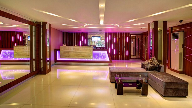 A modern lobby with a reception desk, seating area, and a television screen. - Vio Veteran (Bandung)