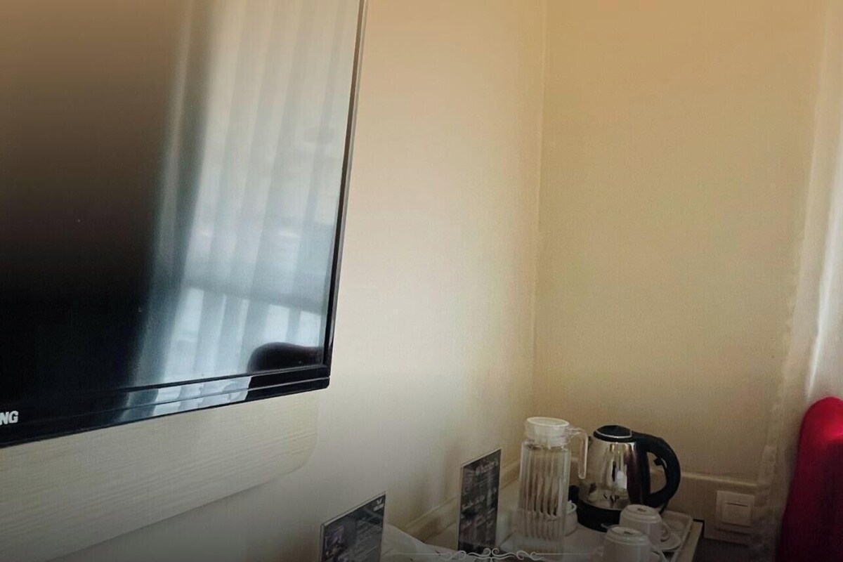 A hotel room with a TV mounted on the wall, a coffee maker, and a red chair.