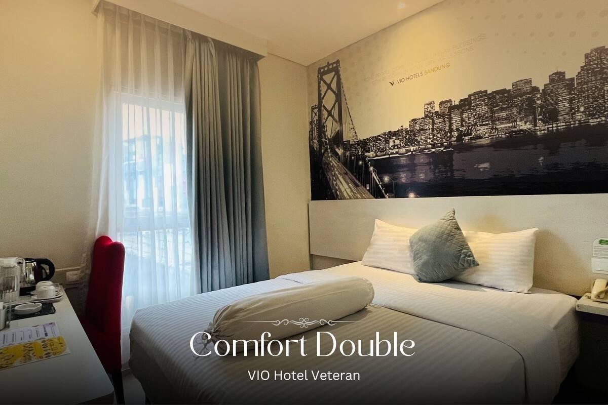 A hotel room with a bed, a desk with a coffee maker, and a cityscape mural on the wall.