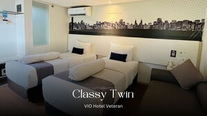 A hotel room with twin beds, a cityscape mural, and a VIO Hotel Veteran sign. - Vio Veteran (Bandung)
