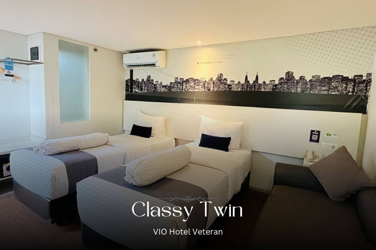 A hotel room with twin beds, a cityscape mural, and a VIO Hotel Veteran sign.