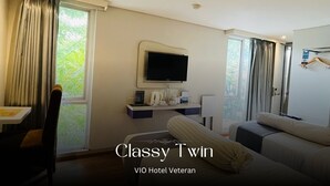 A hotel room with a bed, a desk with a chair, a television, and a window with curtains. - Vio Veteran (Bandung)