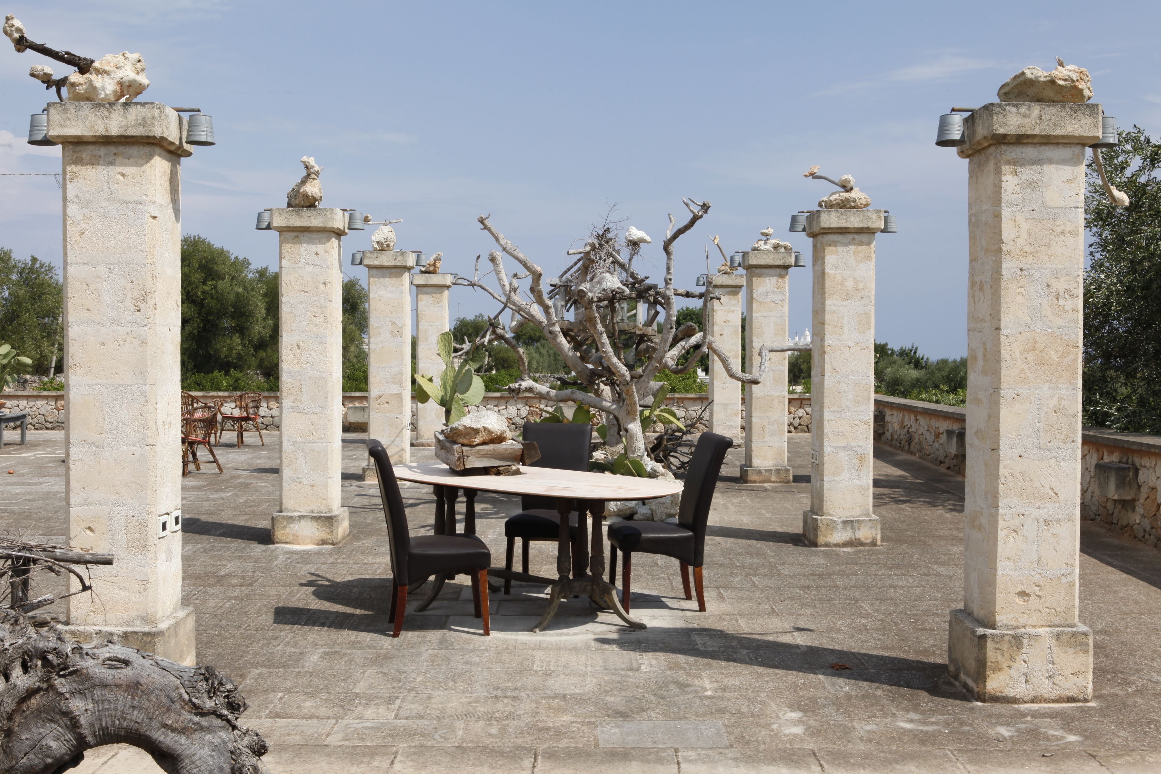 Un patio de piedra con una mesa redonda y sillas, rodeado de columnas con estatuas.