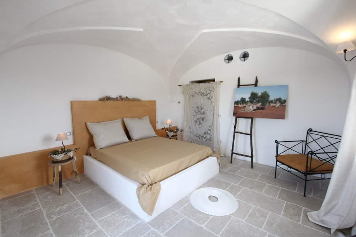 Une chambre à coucher avec un lit, une petite table avec une lampe, une chaise et un tableau accroché au mur.