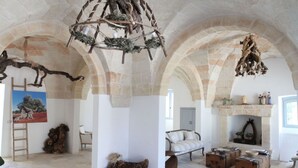 A spacious room with stone arches, a fireplace, and rustic decor including a chandelier and wooden trunks. - Masseria Lama di Coccaro (Fasano)