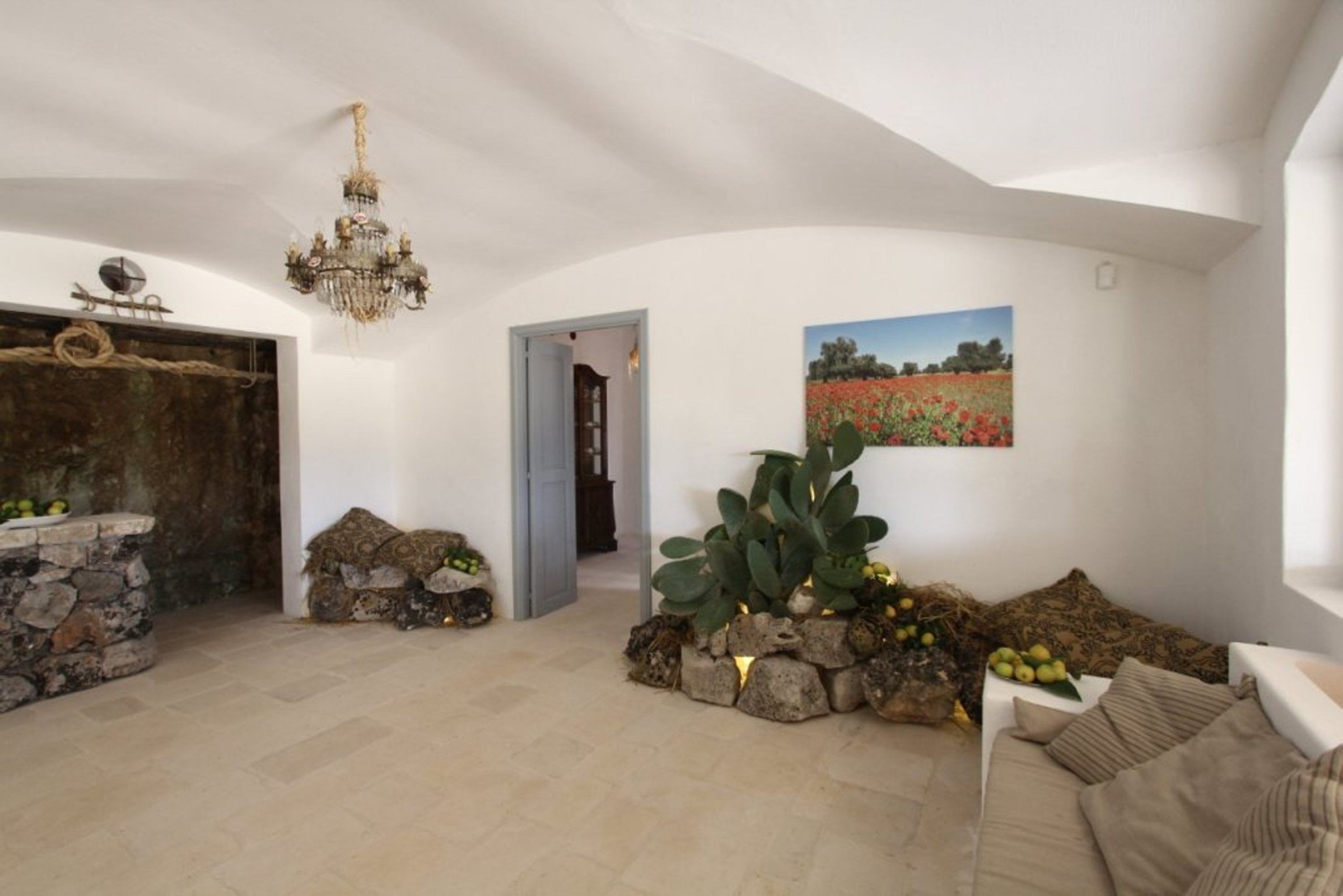 A spacious living area with a stone fireplace, a chandelier, and a large cactus plant.