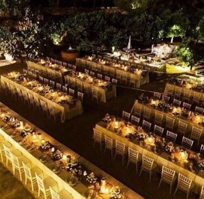 Un salón para banquetes al aire libre con varias mesas redondas y sillas, rodeado de follaje.