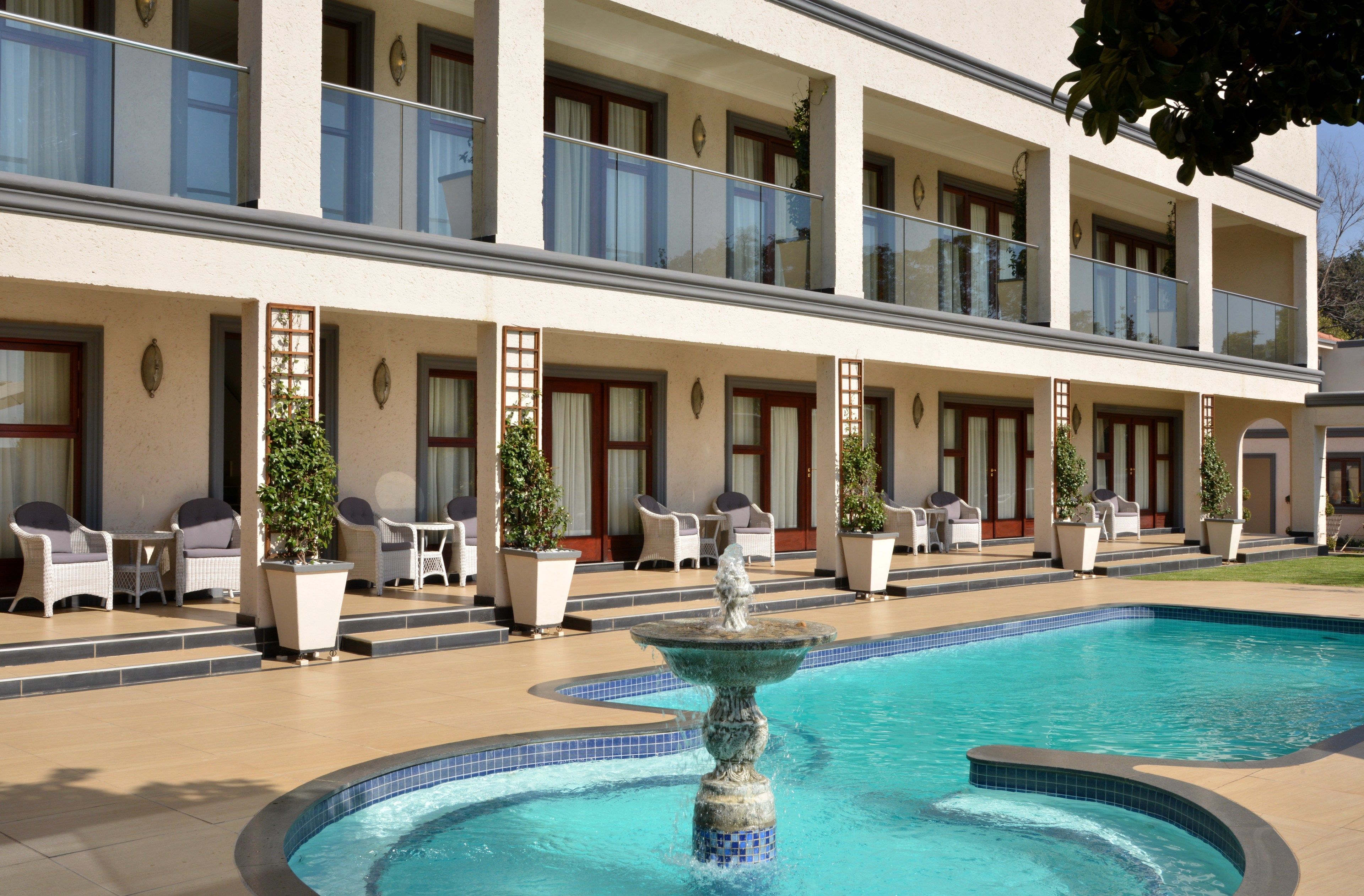 Un hotel con piscina, mobiliario exterior y una fuente.