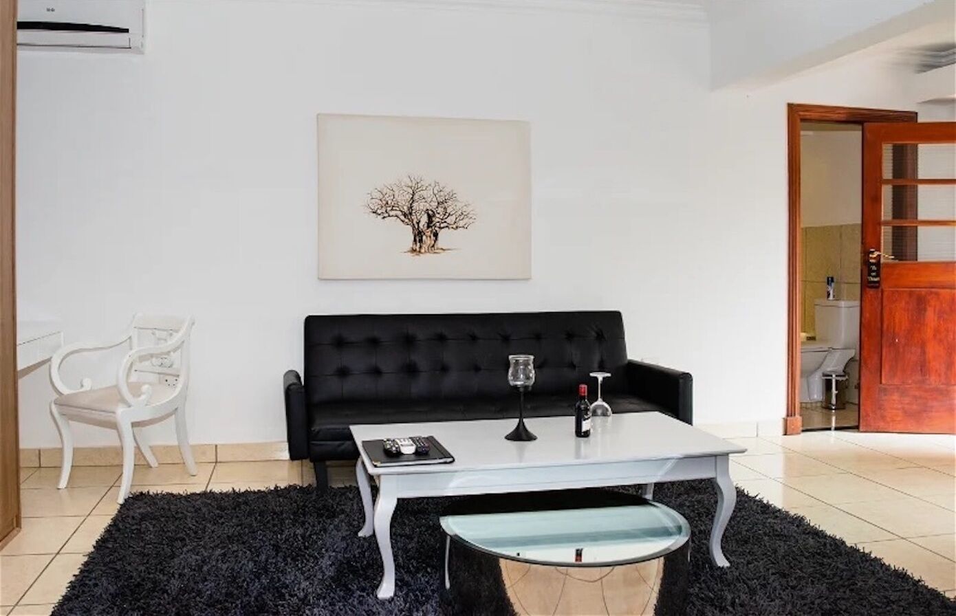 A living room with a black sofa, a white coffee table, a framed picture on the wall, and a door leading to another room.