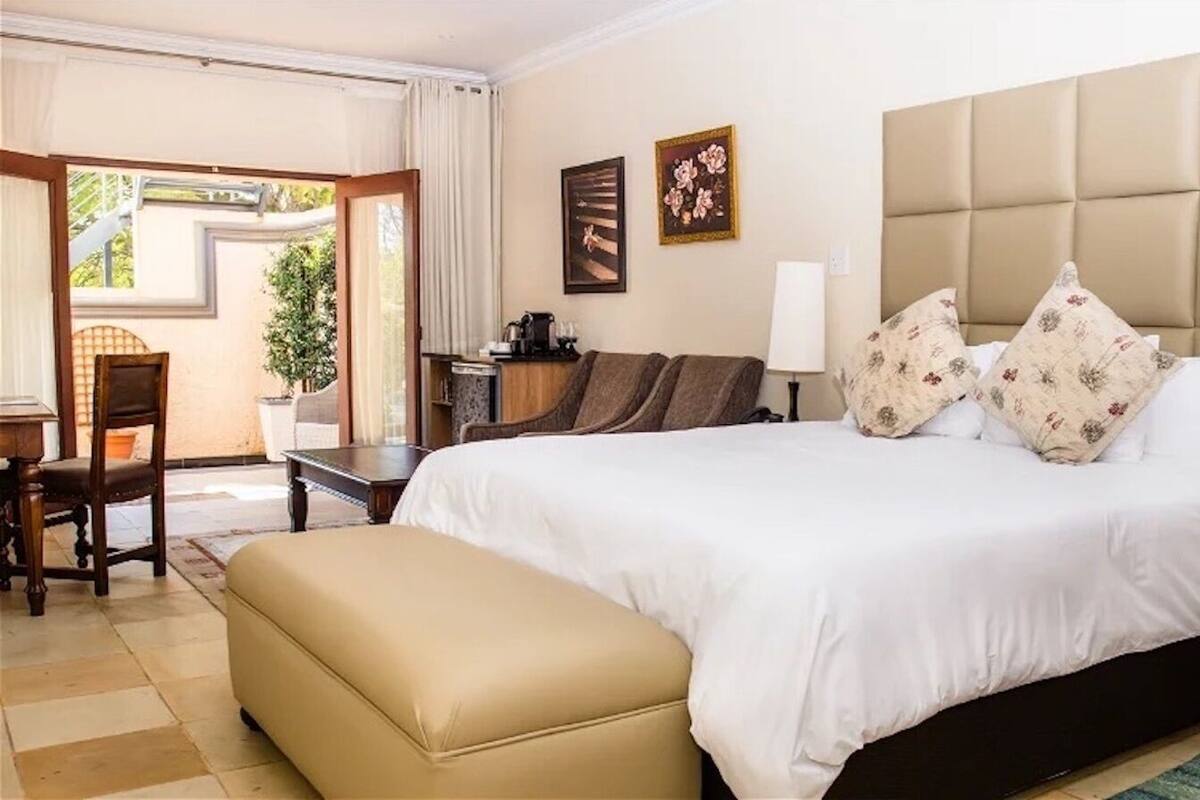 Quarto de hotel com uma cama grande, mesa de cabeceira, uma cadeira, escrivaninha e janela com cortinas.