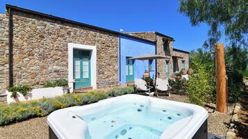 A stone building with a hot tub in the foreground, outdoor seating, and a clear blue sky.