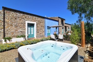 A stone building with a hot tub in the foreground, outdoor seating, and a clear blue sky. - Terre di Himera (Termini Imerese)