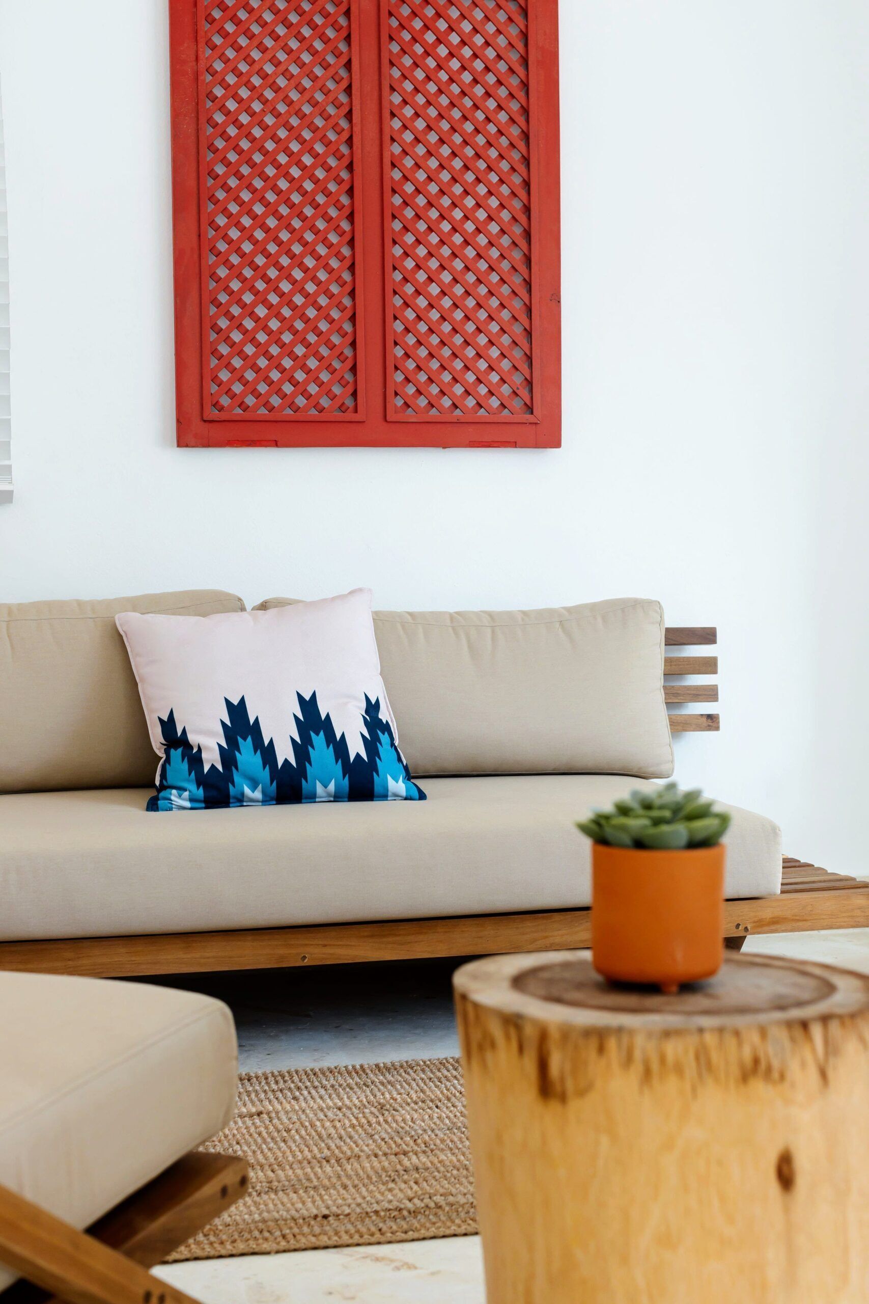 A modern living room with a beige sofa, a patterned pillow, a small potted plant, and a wooden side table.