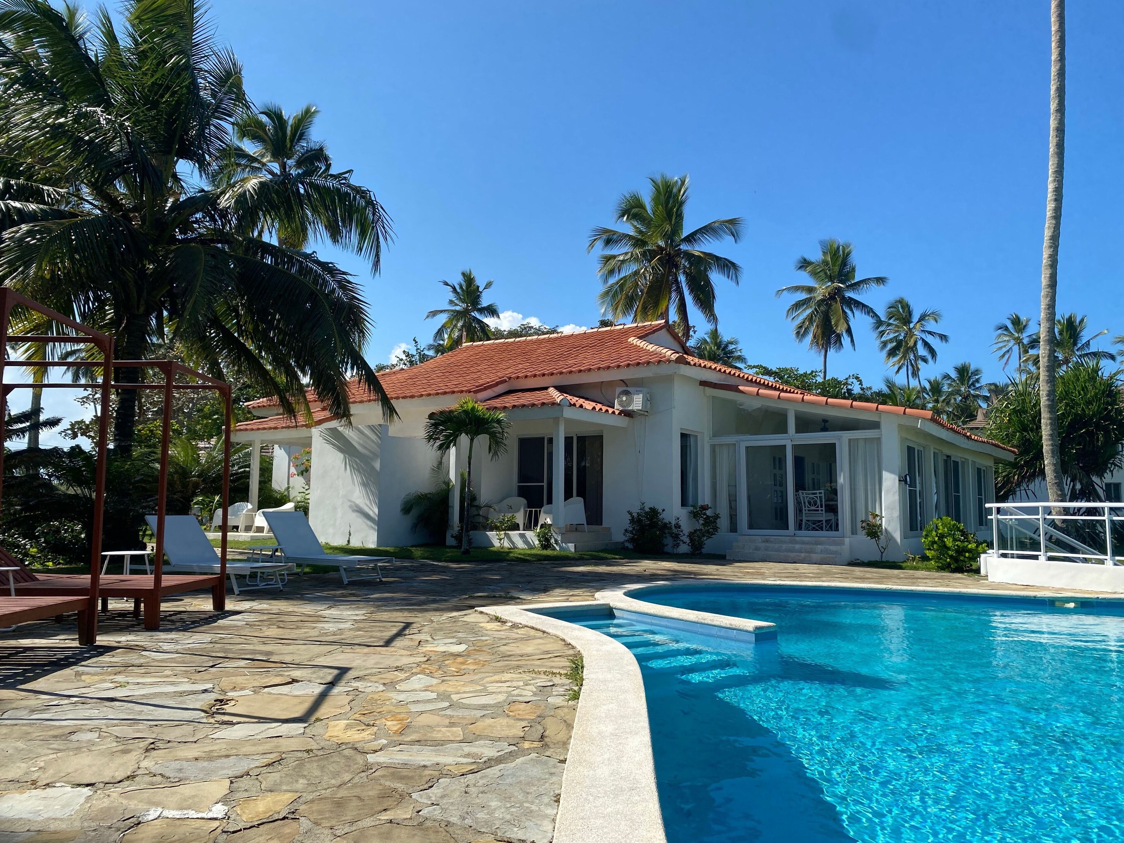 A house with a swimming pool, surrounded by palm trees and a stone patio.