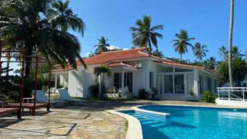 A house with a swimming pool, surrounded by palm trees and a stone patio.