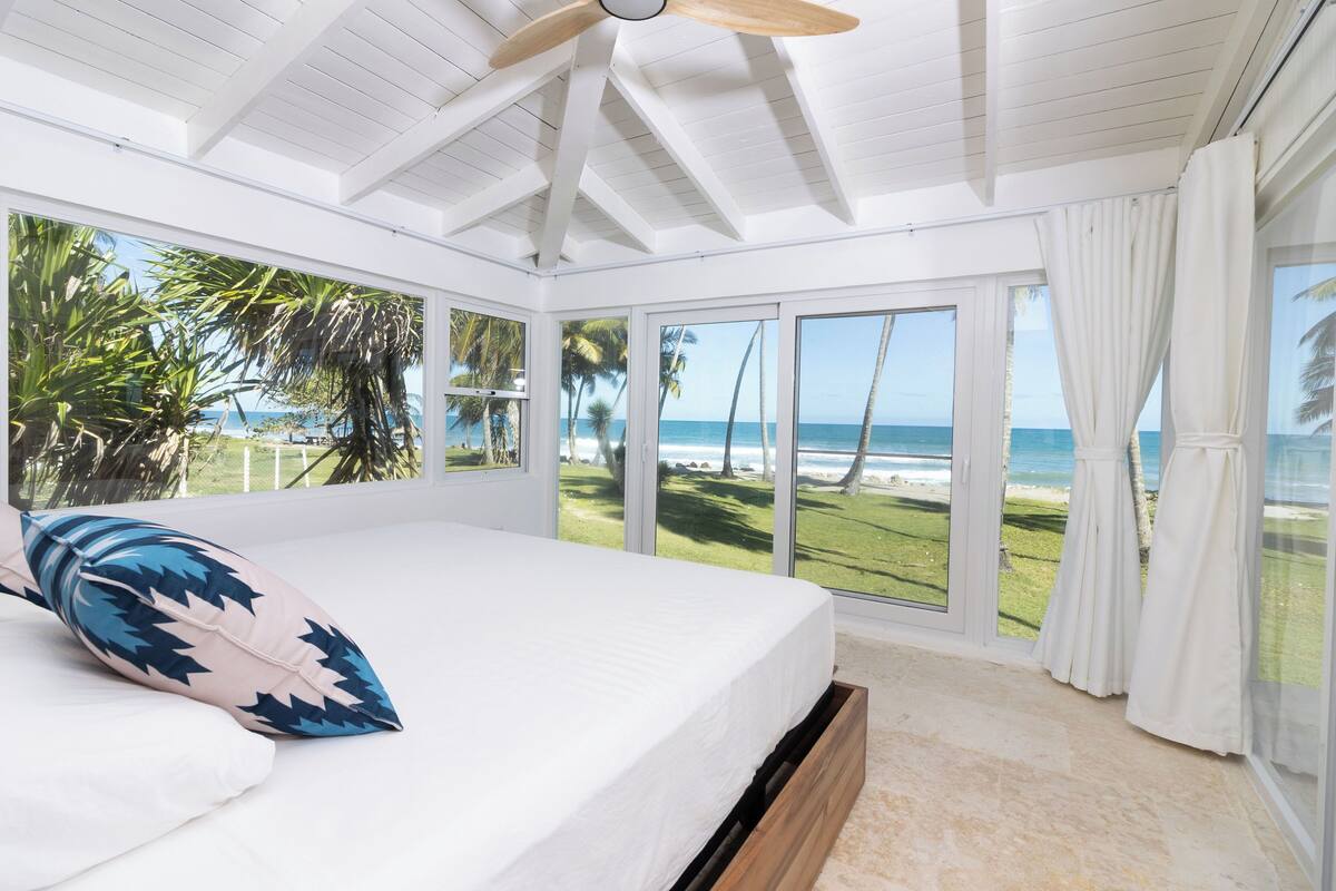 A bedroom with a large bed, a ceiling fan, and a view of the beach.
