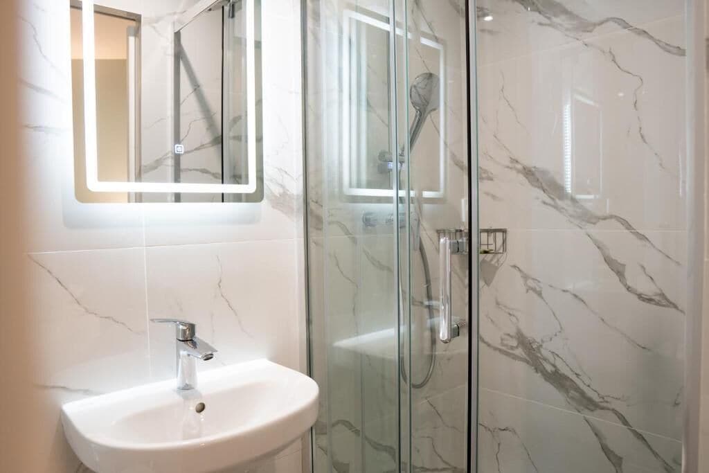 Une salle de bain avec une douche à parois de verre, un lavabo blanc et un miroir doté d’un cadre éclairé.