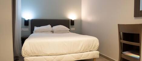 A neatly made bed with white bedding, a dark headboard, and two wall-mounted nightstands with lamps.