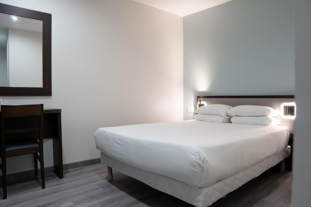 A hotel room with a bed, a desk, and a chair.