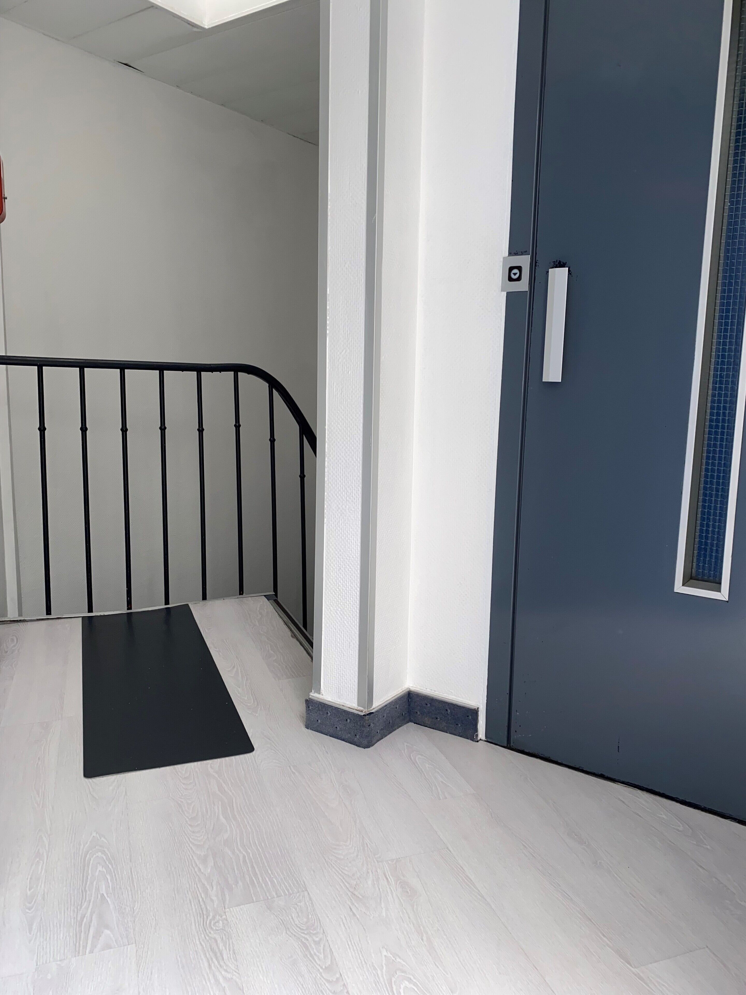 A modern interior with a staircase, a door with a window, and a textured wall.
