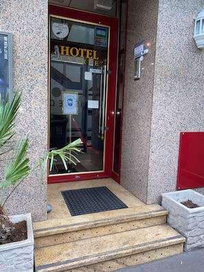 Entrada de hotel con puerta roja, ventana de vidrio y aviso de vigilancia.