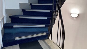 A staircase with blue carpeted steps and a black handrail, leading to a landing with a light fixture. - Aéro Club (Issy-les-Moulineaux)