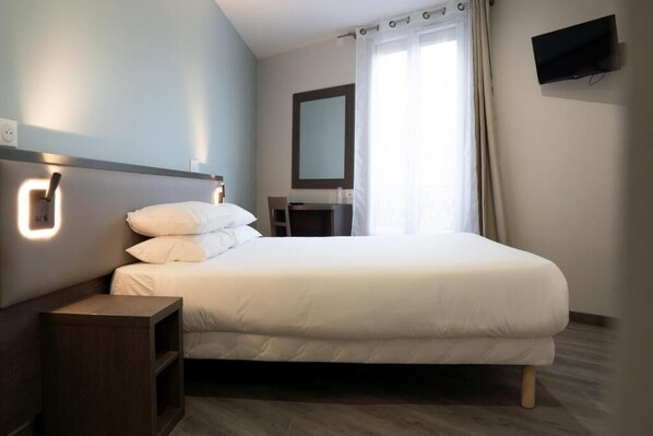 Una habitación de hotel moderna con una cama grande, mesita de noche y un televisor de pantalla plana montado en la pared.