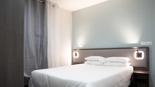 A neatly made bed with white linens in a room with light blue walls and a wooden headboard. - Aéro Club (Issy-les-Moulineaux)
