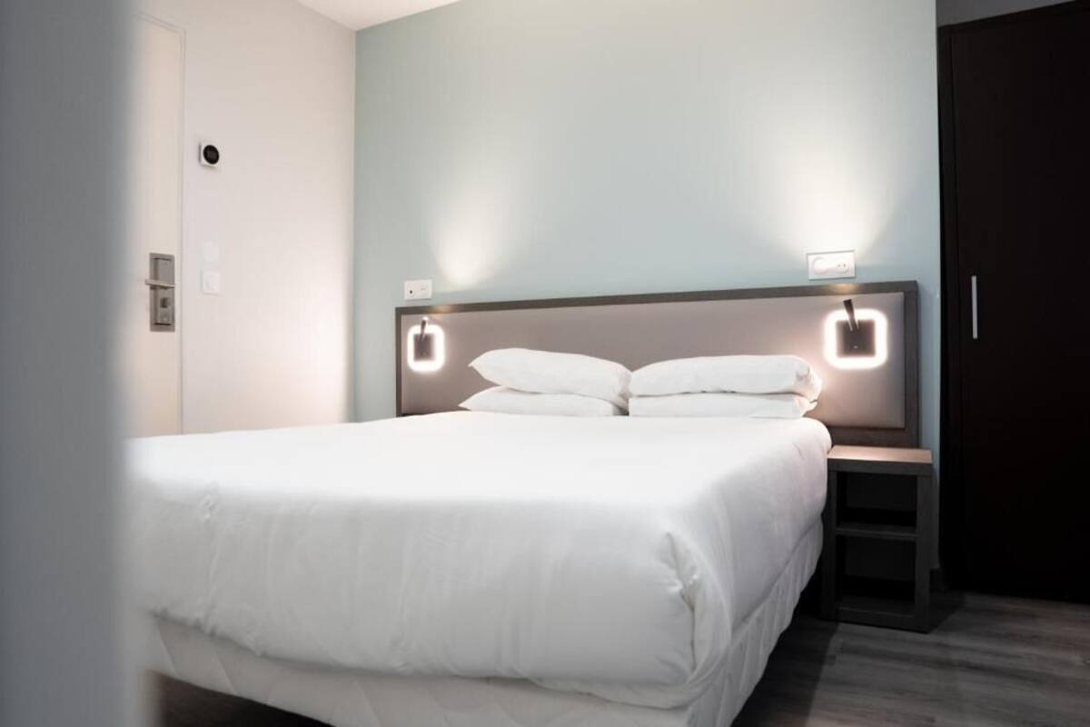 Siististi pedattu sänky valkoisilla vuodevaatteilla modernissa hotellihuoneessa.