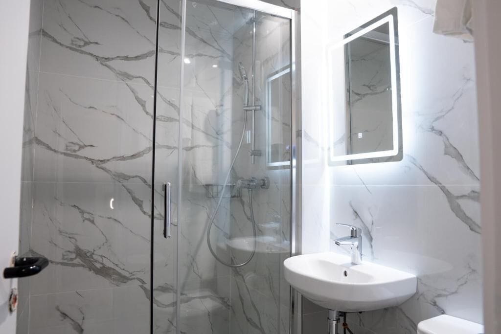 A modern bathroom with a glass-enclosed shower, a white sink, and a marble-tiled wall.