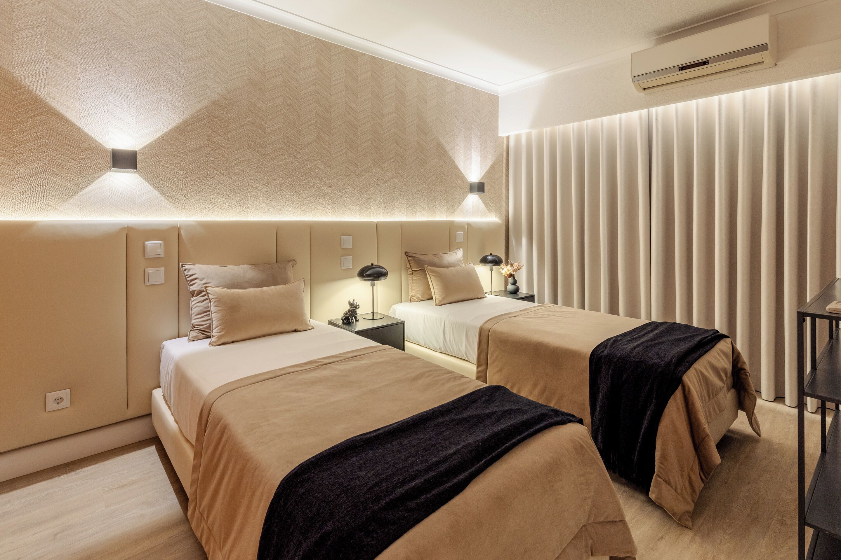 Ein Hotelzimmer mit zwei Betten, einem großen Fenster mit Jalousien, einer Klimaanlage und einem Nachttisch mit Lampe.