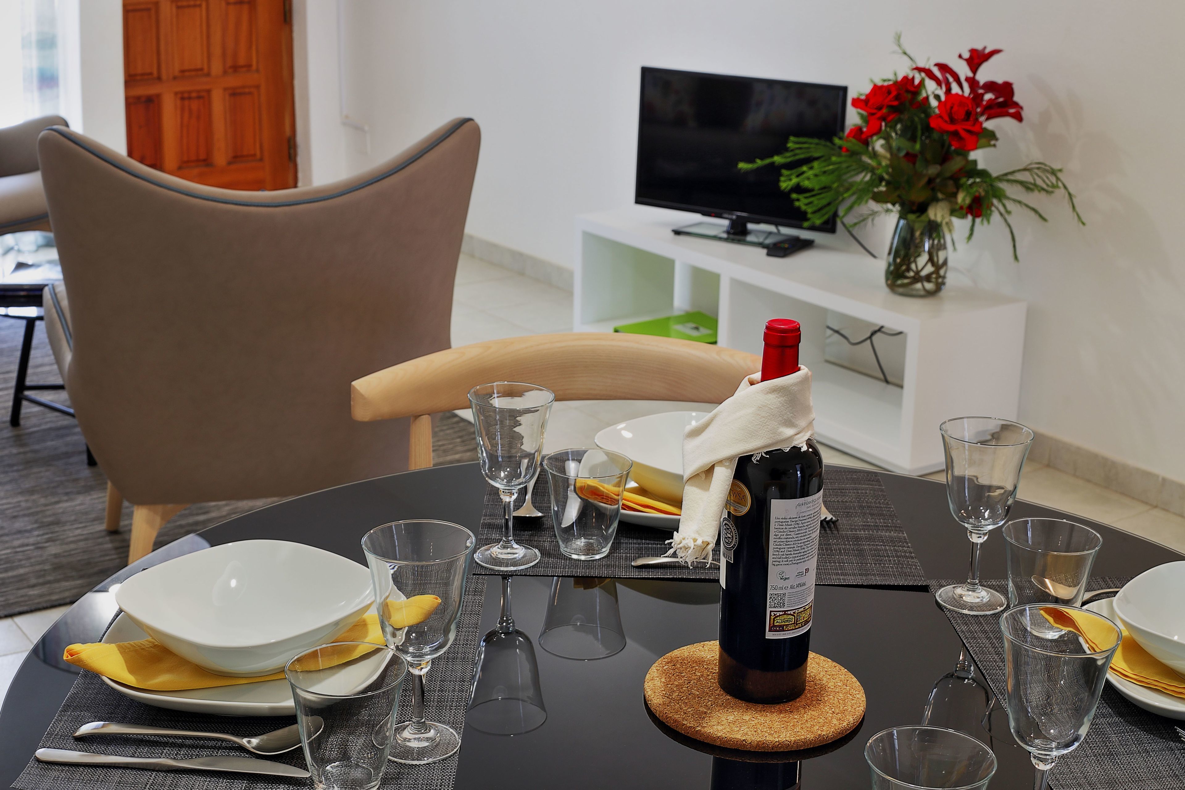 A dining table set with a bottle of wine, glasses, plates, and a bowl.
