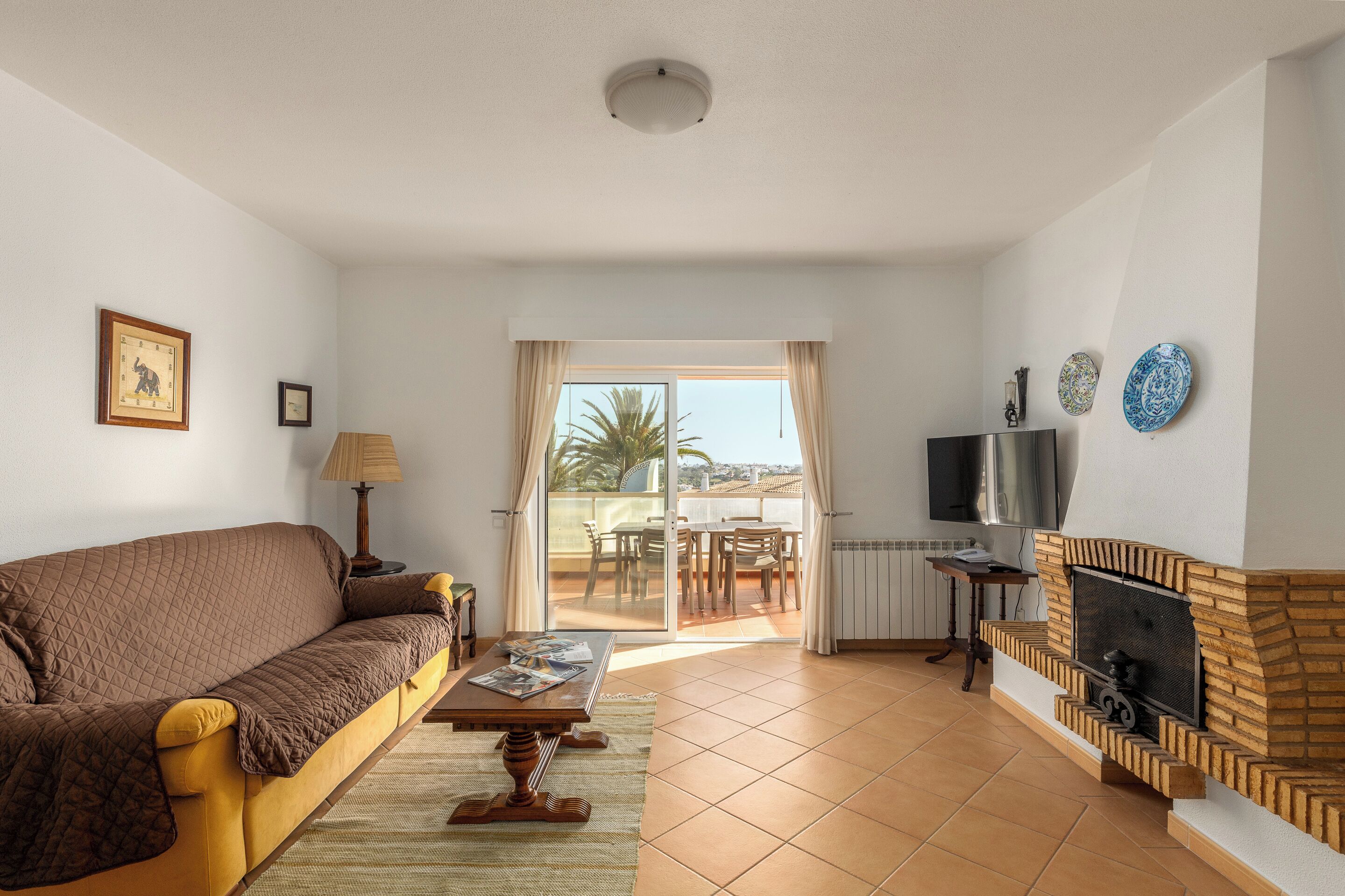 Uma sala de estar com sofá, mesa de centro, televisão, lareira e varanda com mesa e cadeiras.