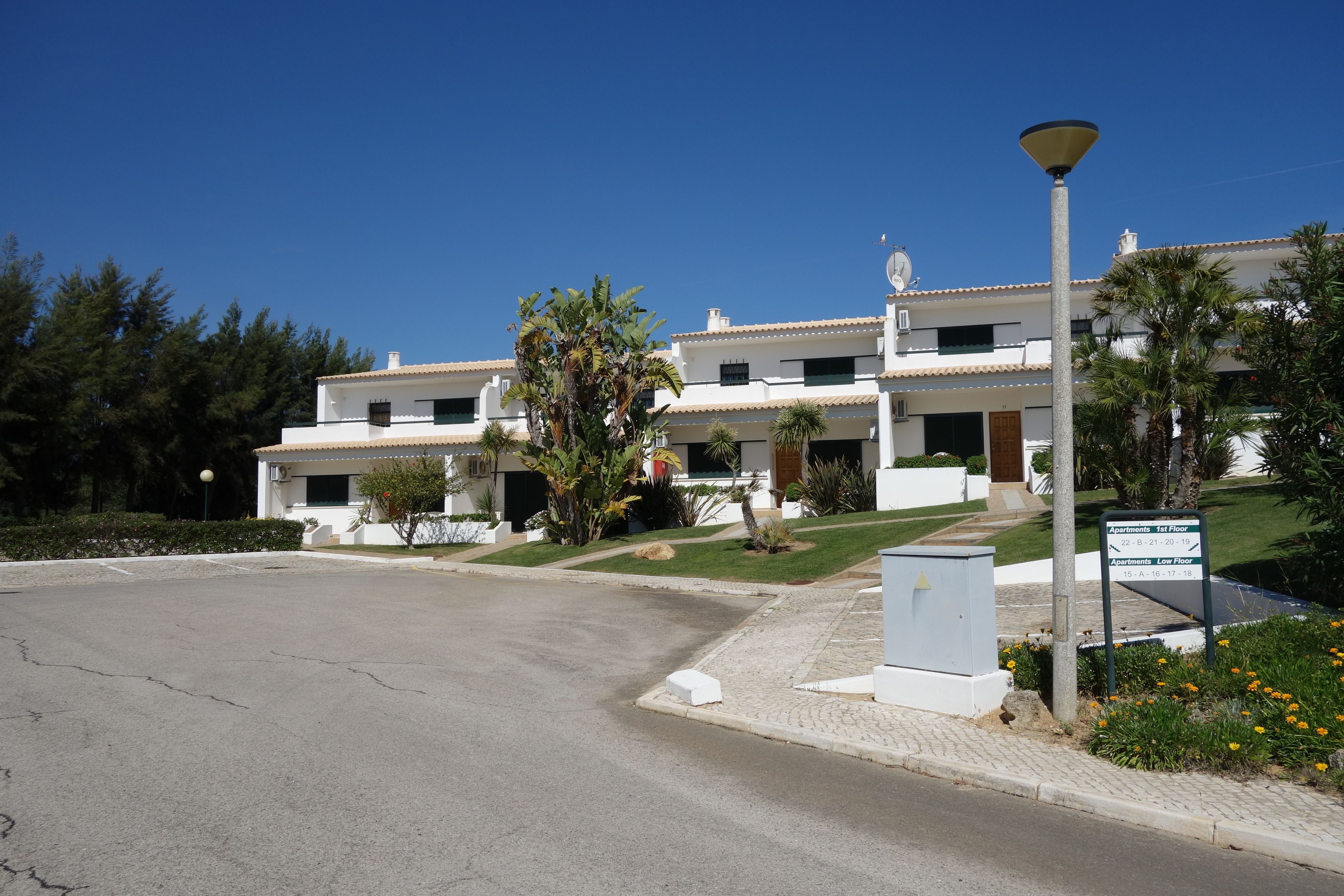 A modern apartment building with a clear driveway, a well-maintained lawn, and a sign indicating the availability of apartments on the first and low floors.