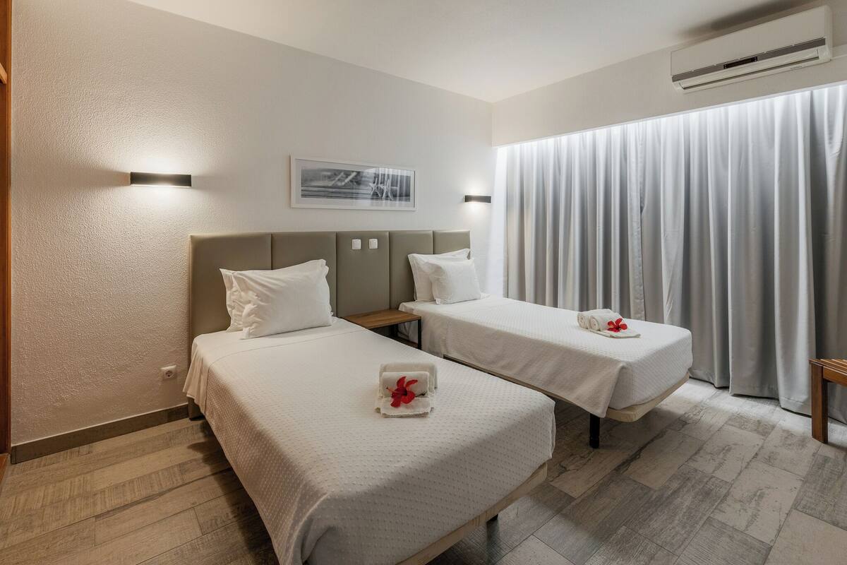 Habitación de hotel con dos camas, una mesita, aire acondicionado de pared y una ventana con cortinas.