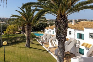 A white building with a tiled roof, a swimming pool, and palm trees.