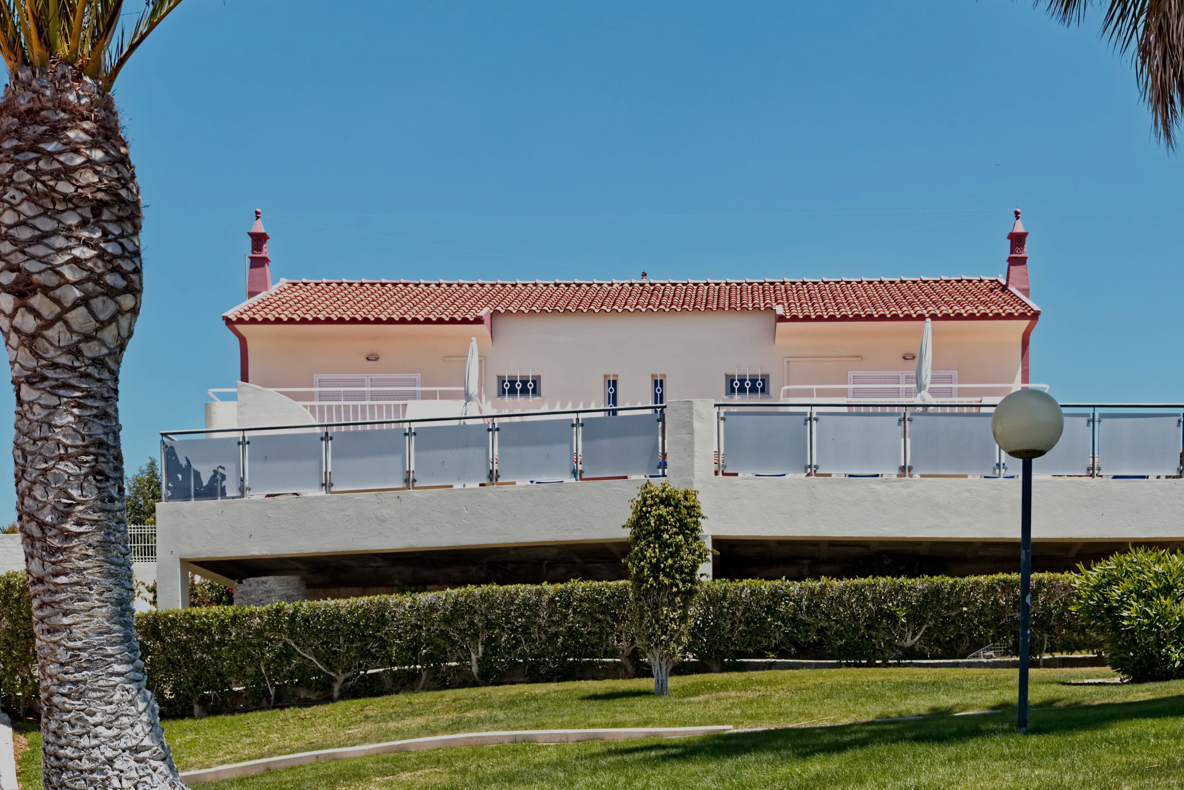 A two-story building with a red-tiled roof, a balcony with glass railings, and a clear blue sky.