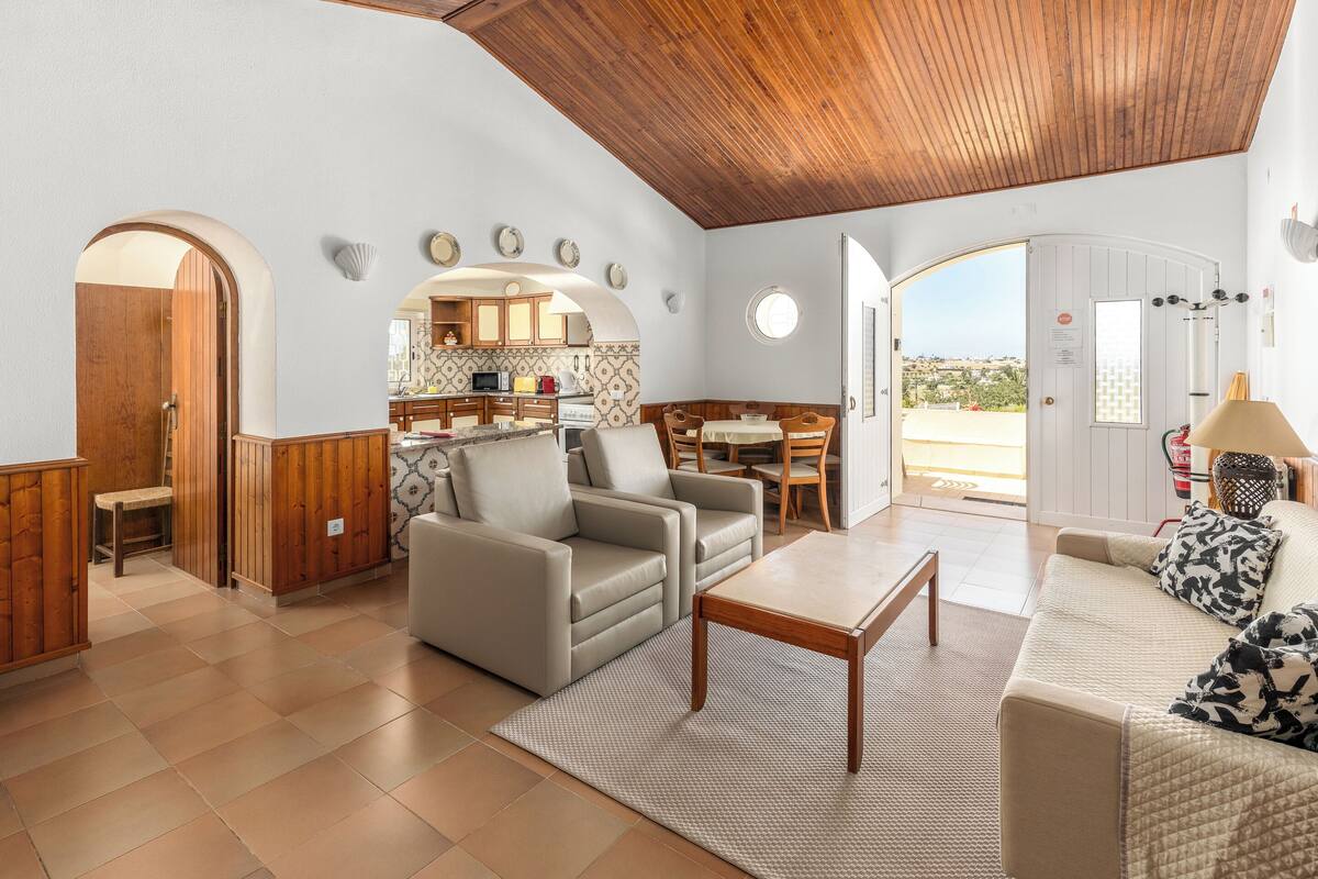 Amplia sala de estar con techo de madera, un sofá, una mesa de centro y vistas a la cocina y al exterior.
