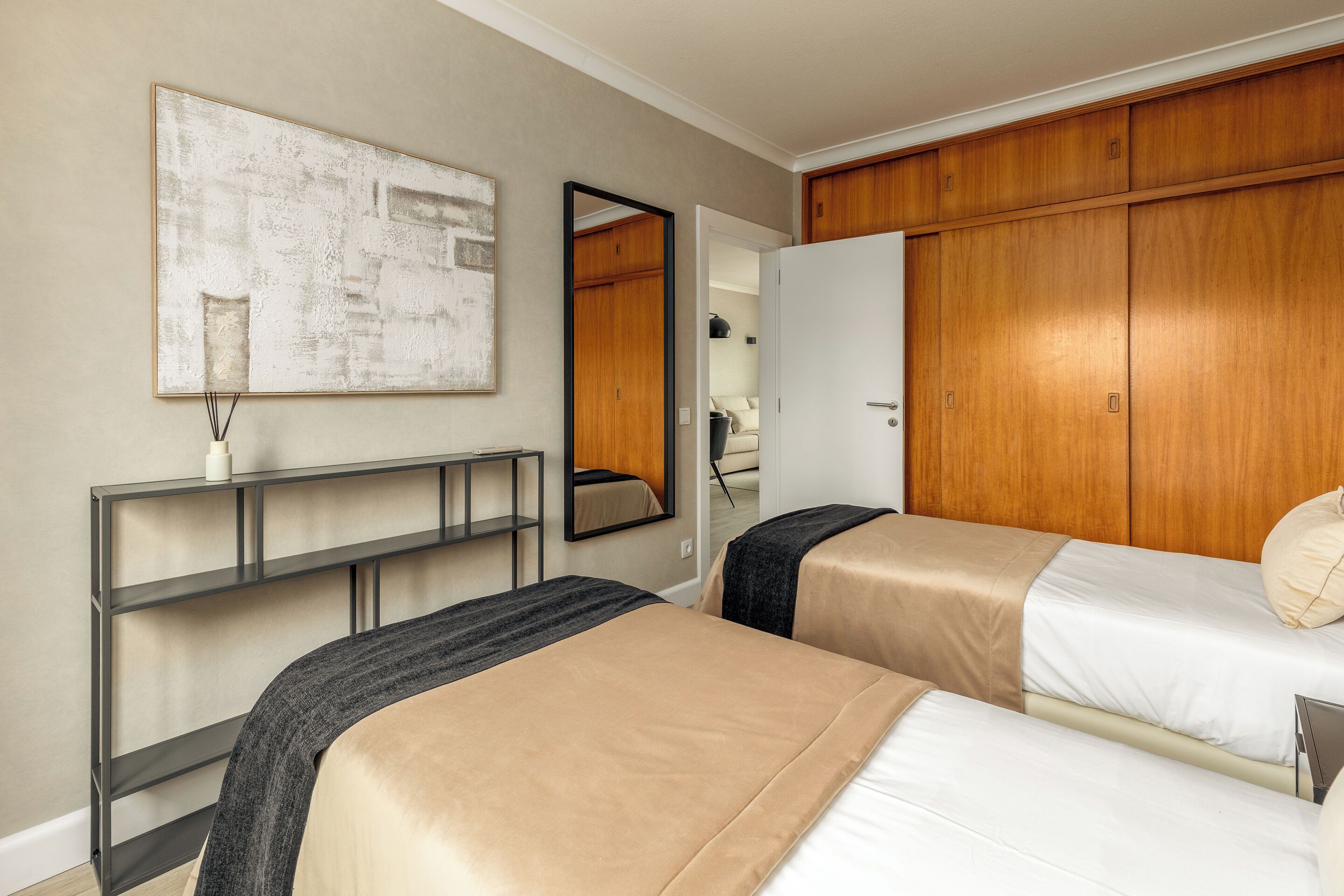 Quarto de hotel com duas camas, um espelho grande, um guarda-roupa de madeira e uma obra de arte moderna na parede.