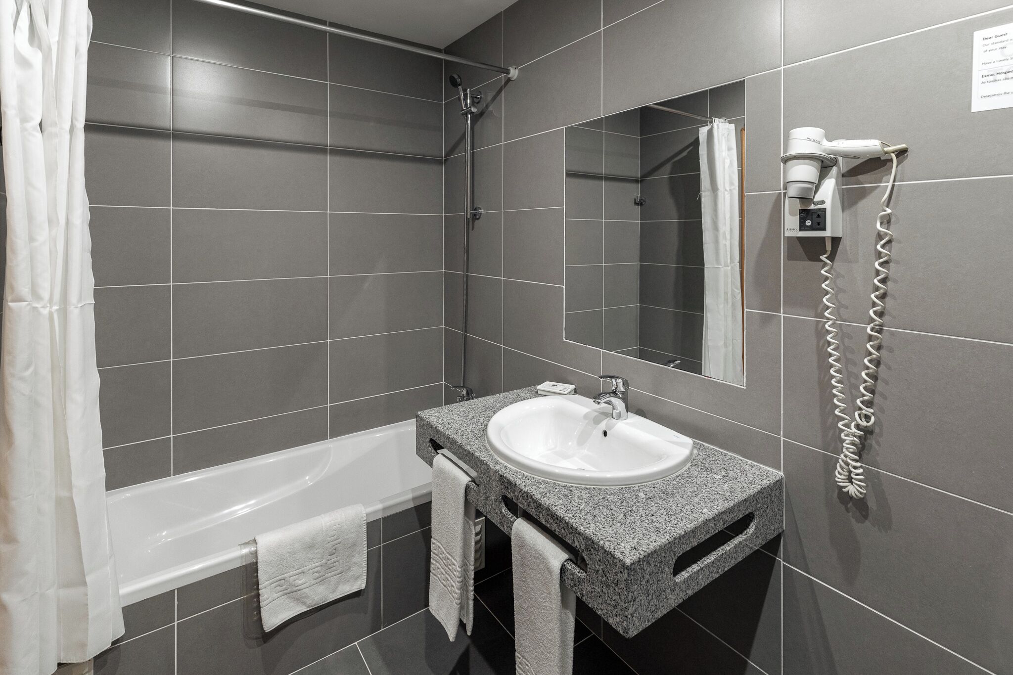 Een moderne badkamer met een bad, een wastafel en een aan de muur bevestigde haardroger.