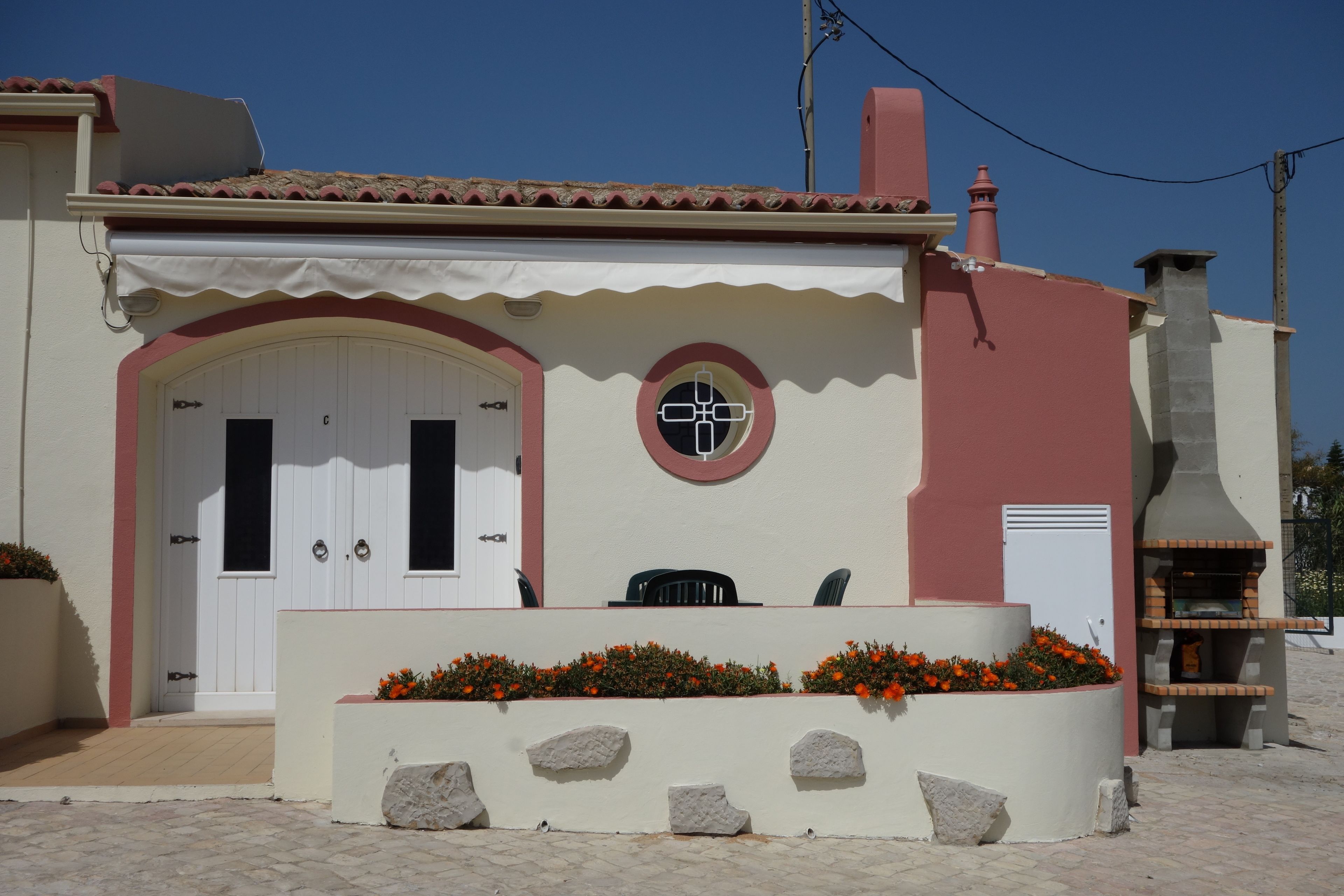 Une maison avec une porte blanche, un petit porche doté d’un banc et un four en briques.