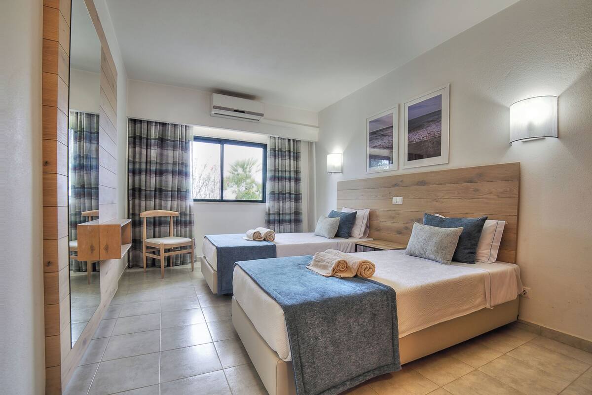 Una habitación de hotel con dos camas, un escritorio, una silla, un espejo y una ventana con cortinas.