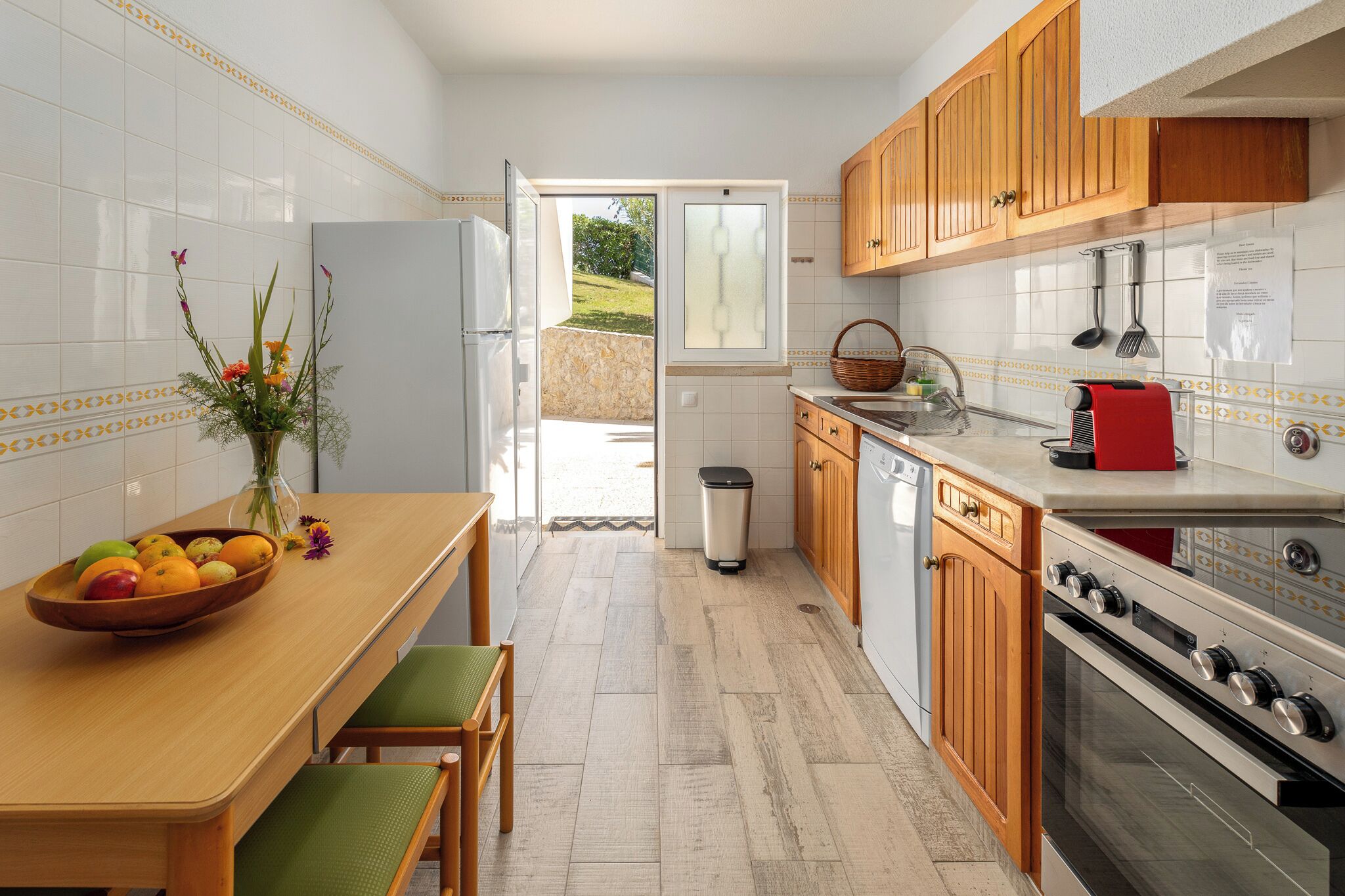 Una cocina con una mesa de madera, un frutero, un cubo de basura y vistas al exterior.