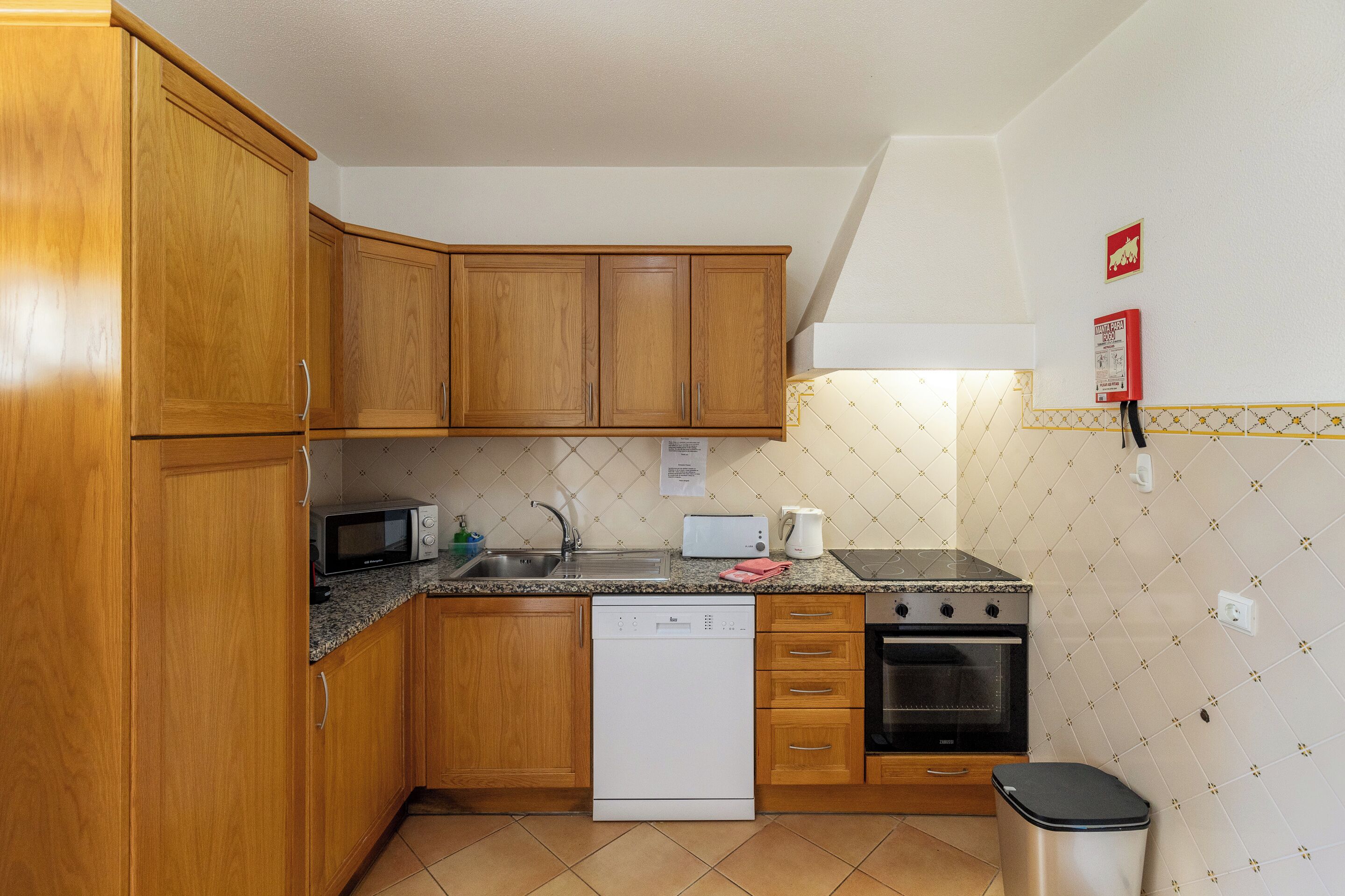 A compact kitchen with wooden cabinets, a microwave, a toaster, a dishwasher, and a stove.