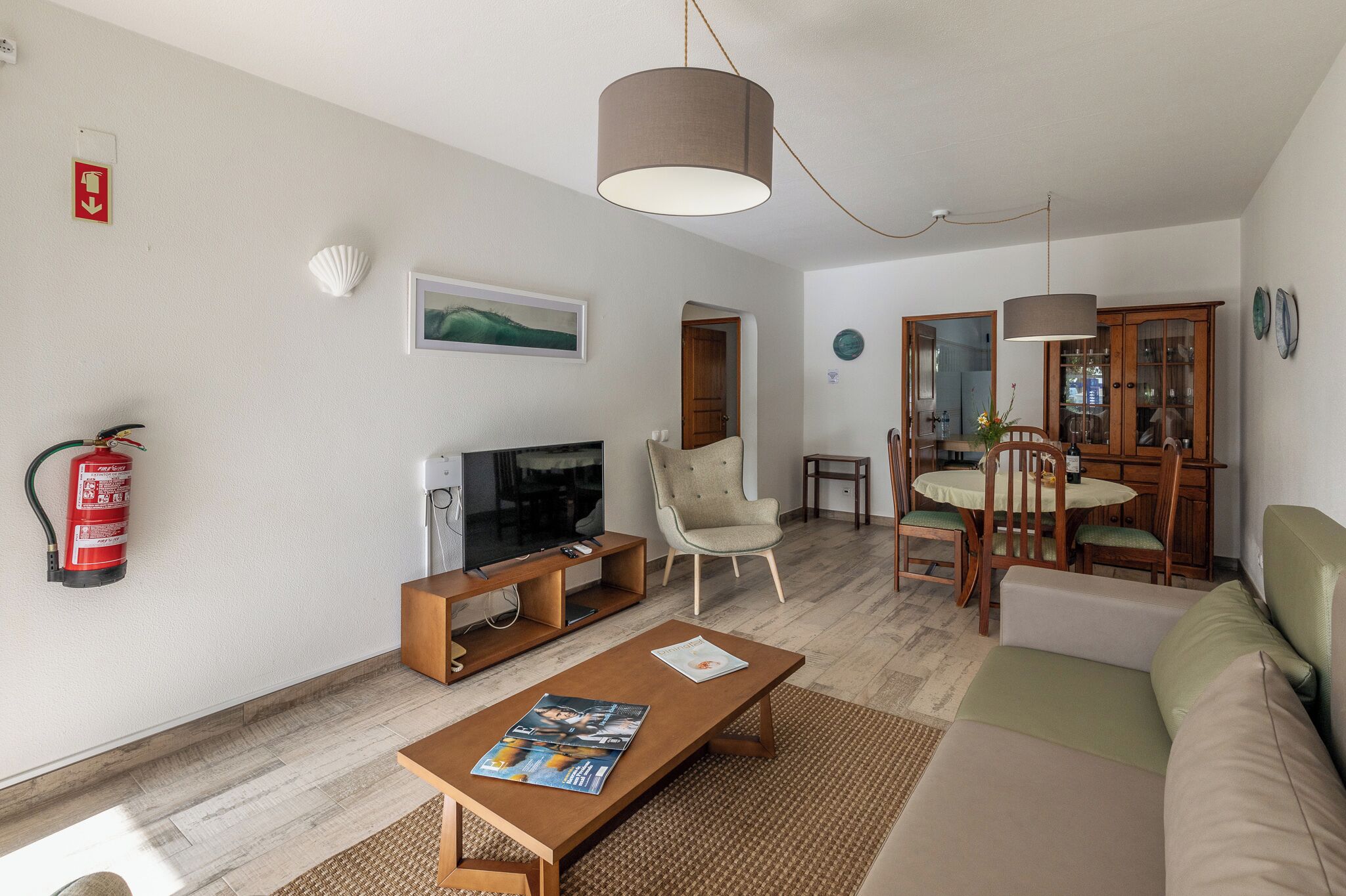 A living room with a TV, sofa, coffee table, and dining area with chairs and a table.