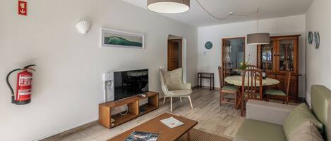 A living room with a TV, sofa, coffee table, and dining area with chairs and a table.