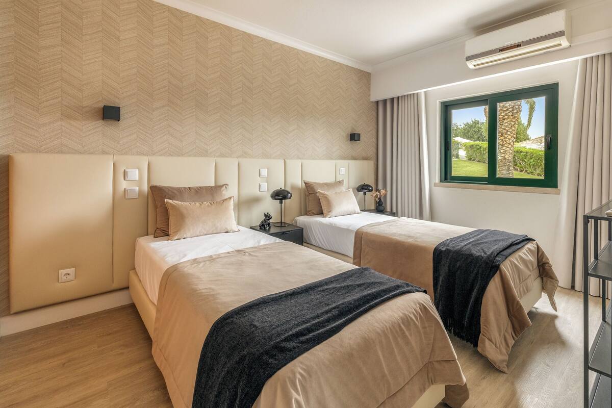 Habitación de hotel con dos camas, un ventanal con vistas a zonas verdes, aire acondicionado de pared y diseño moderno.