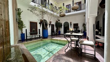 A courtyard with a pool, outdoor seating, and potted plants.