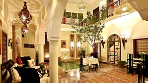 A spacious lobby with a high ceiling, a chandelier, a dining area, and a staircase leading to an upper level. - Le Riad Jardin Des Rêves By La Siredrah (Marrakech)
